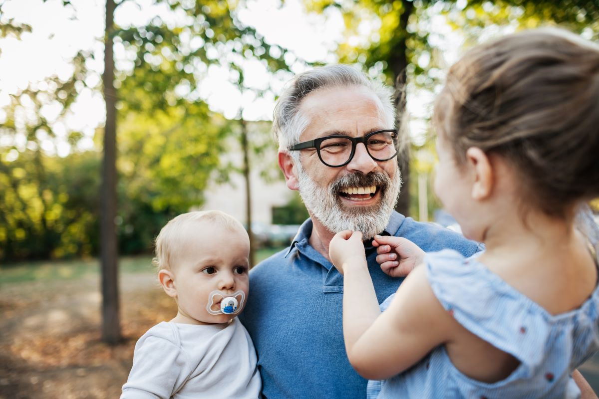 grandfather wearing glasses holding infant and young child